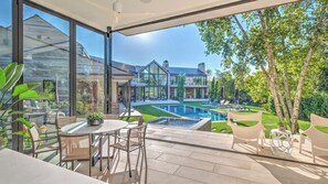 A modern outdoor patio with a pool, seating, and a view of a large house with a swimming pool.