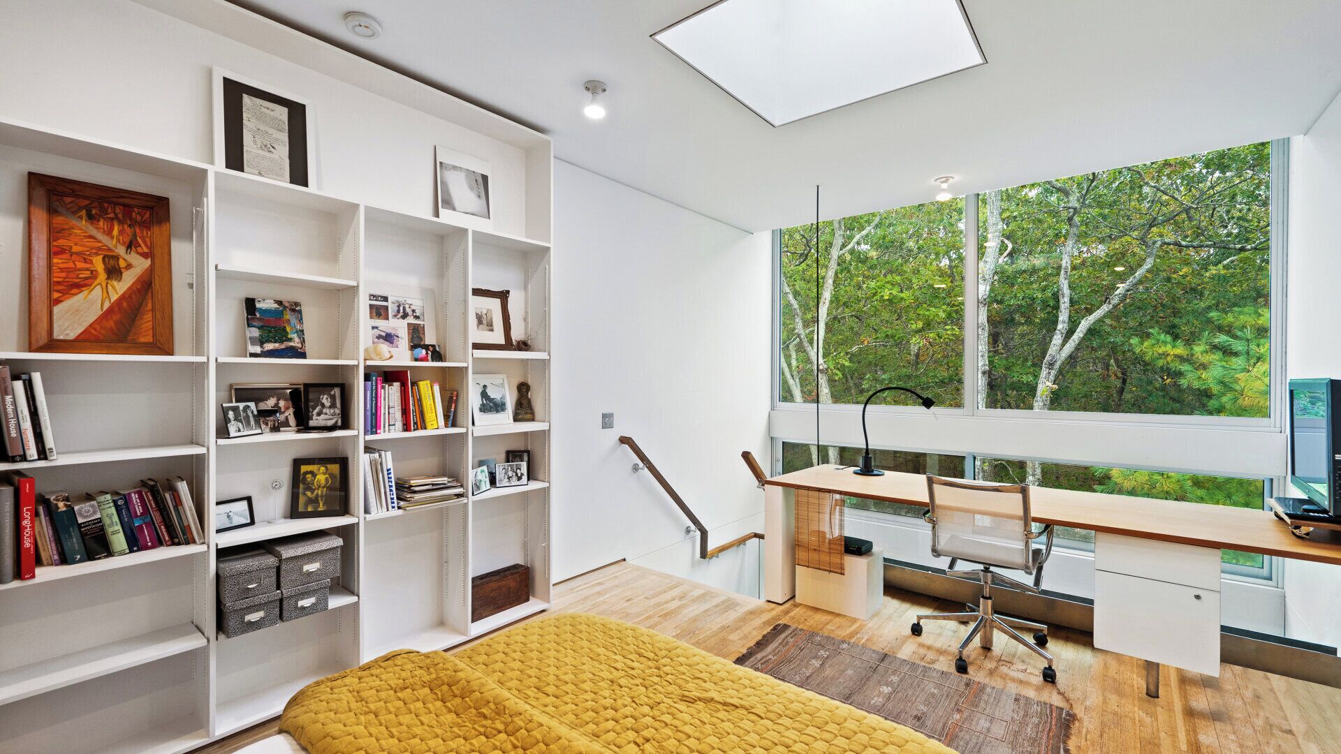 A modern room with a large window, a desk, and a bookshelf filled with books and framed photos.