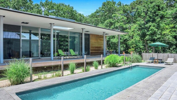 A modern house with a swimming pool, large windows, and outdoor seating. - Modern home sited on a lush wood acre, stunning pool, covered deck, outdoor... (East Hampton)