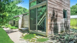 A modern, multi-story wooden house with large glass windows and a visible staircase. - Modern home sited on a lush wood acre, stunning pool, covered deck, outdoor... (East Hampton)