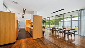 A modern kitchen with wooden cabinets and a dining area with a large table and chairs. - Modern home sited on a lush wood acre, stunning pool, covered deck, outdoor... (East Hampton)