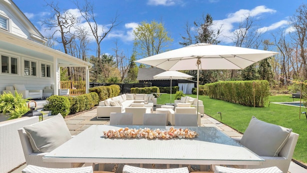 A patio with white wicker furniture, a glass table with seashells, and a large white umbrella. - Beautiful Shelter Island Getaway on over an acre, minutes from the ferry! (Shelter Island)