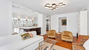 A modern living room with a white sofa, two armchairs, a coffee table, and a kitchen in the background. - Beautiful Shelter Island Getaway on over an acre, minutes from the ferry! (Shelter Island)