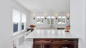 A modern kitchen with a large island, white cabinetry, and a view of the outdoors through the windows. - Beautiful Shelter Island Getaway on over an acre, minutes from the ferry! (Shelter Island)