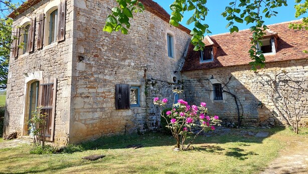 A stone building with a sloped roof, a small garden with pink flowers, and a clear blue sky. - Beautiful Lotoise house, located in a typical village. Large garden and swimming pool. (Le Vignon-en-Quercy)