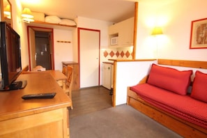 A compact room with a wooden desk, a red sofa, a television, and a microwave.