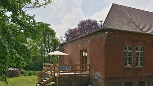 A brick building with a wooden deck and stairs leading to a covered area. - Pure tranquillity: vacation apartment close to nature in Unkengrund (Nordwestuckermark)