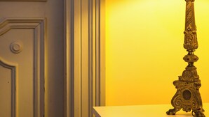 Ein Zimmer mit einem Bett, einer Lampe mit schwarzem Lampenschirm und einer Tür mit Griff.
