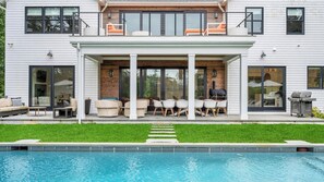 Una casa moderna de dos pisos con porche cubierto, mobiliario exterior y piscina.