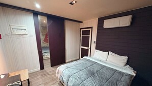 Ein Schlafzimmer mit einem Bett, einem Schreibtisch, einem Kleiderschrank und einer Tür.