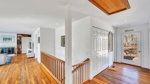 A spacious hallway with wooden flooring, white walls, and a wooden railing. There is a door labeled "Beach" with a view of trees.