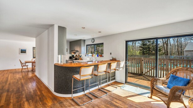 A modern kitchen with a bar area, large windows, and a balcony with wicker furniture.