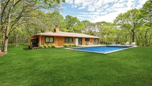 A house with a swimming pool, surrounded by a well-maintained lawn and trees.
