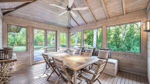 A wooden deck with a table and chairs, large windows, and a ceiling fan.