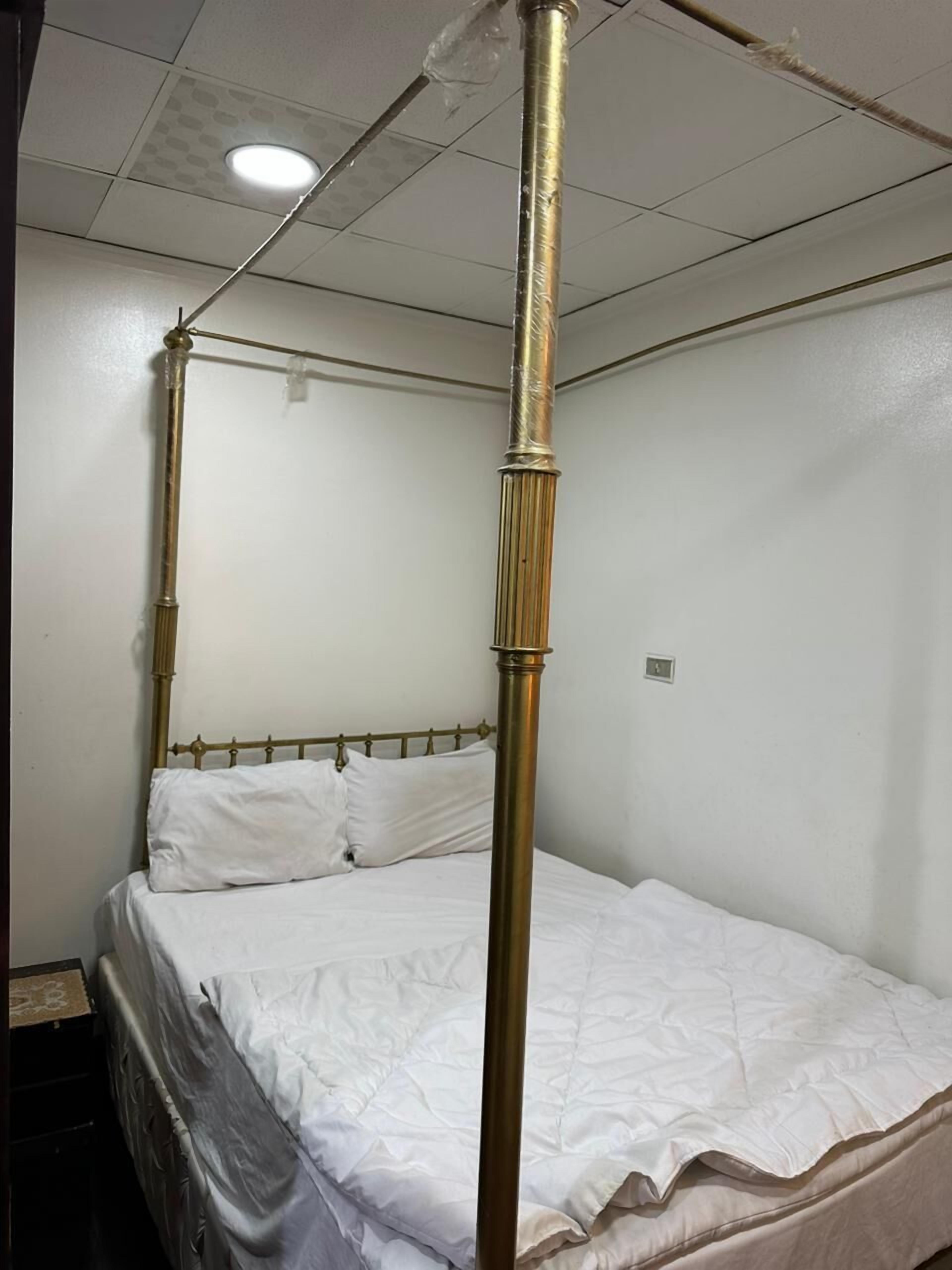 A four-poster bed with white bedding in a room with white walls and a tiled ceiling.