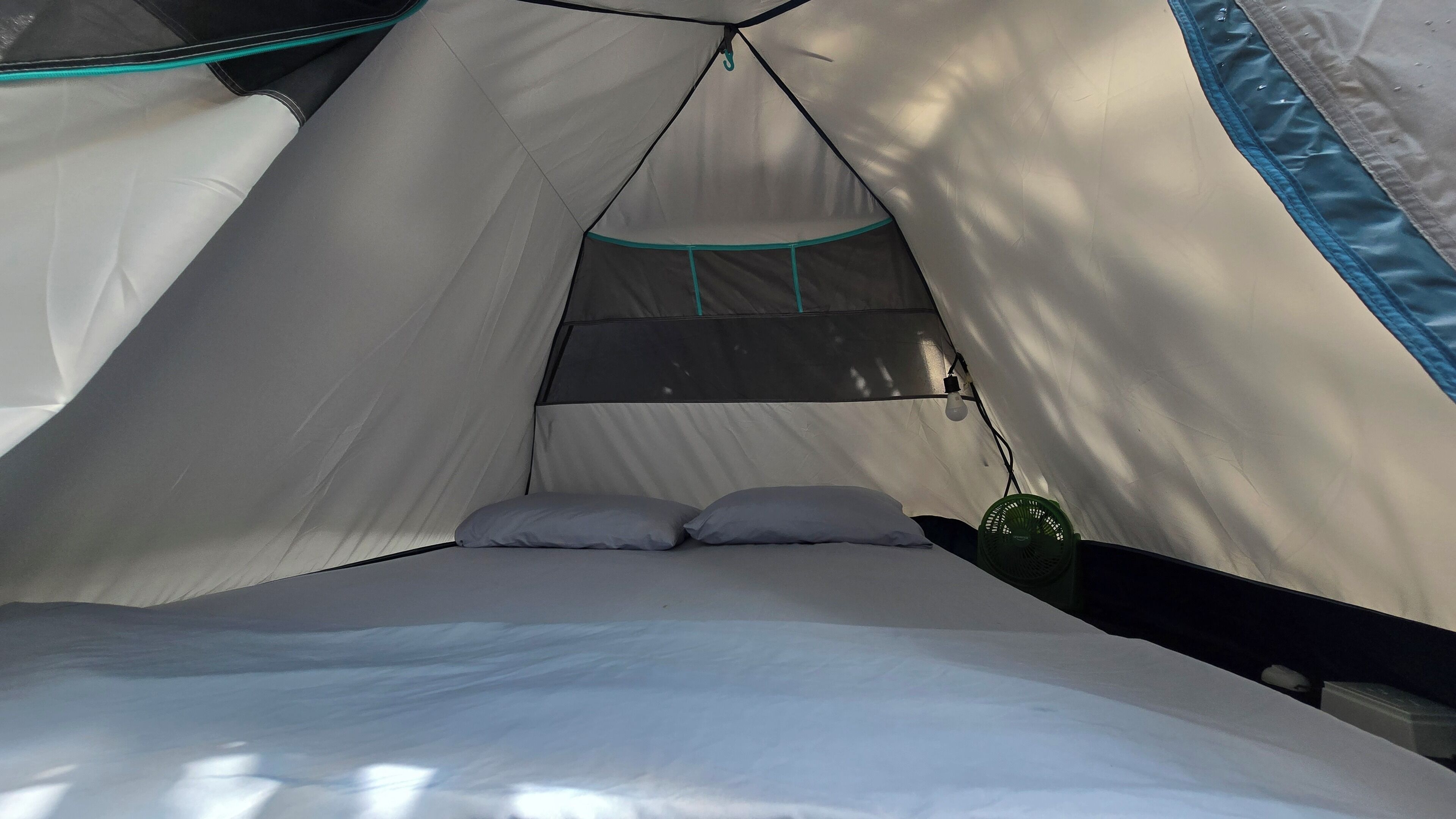 A tent with a bed, pillows, a hanging light, and a fan.