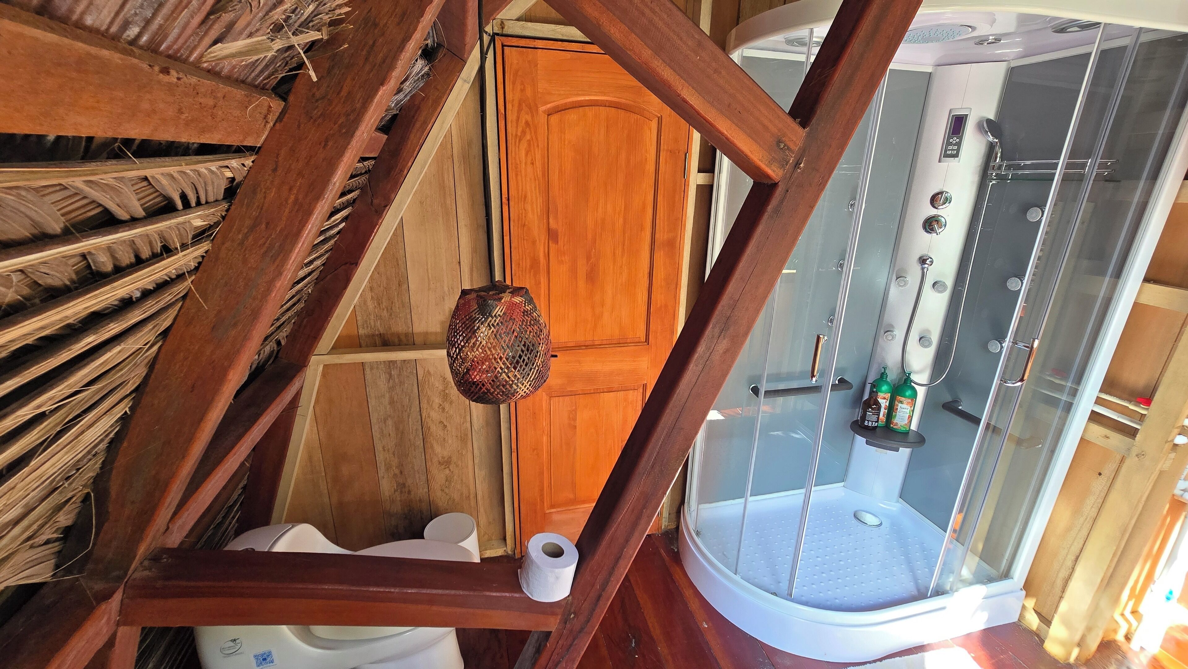 A wooden ceiling with a sloped design, a toilet, a shower stall, and a wooden door.