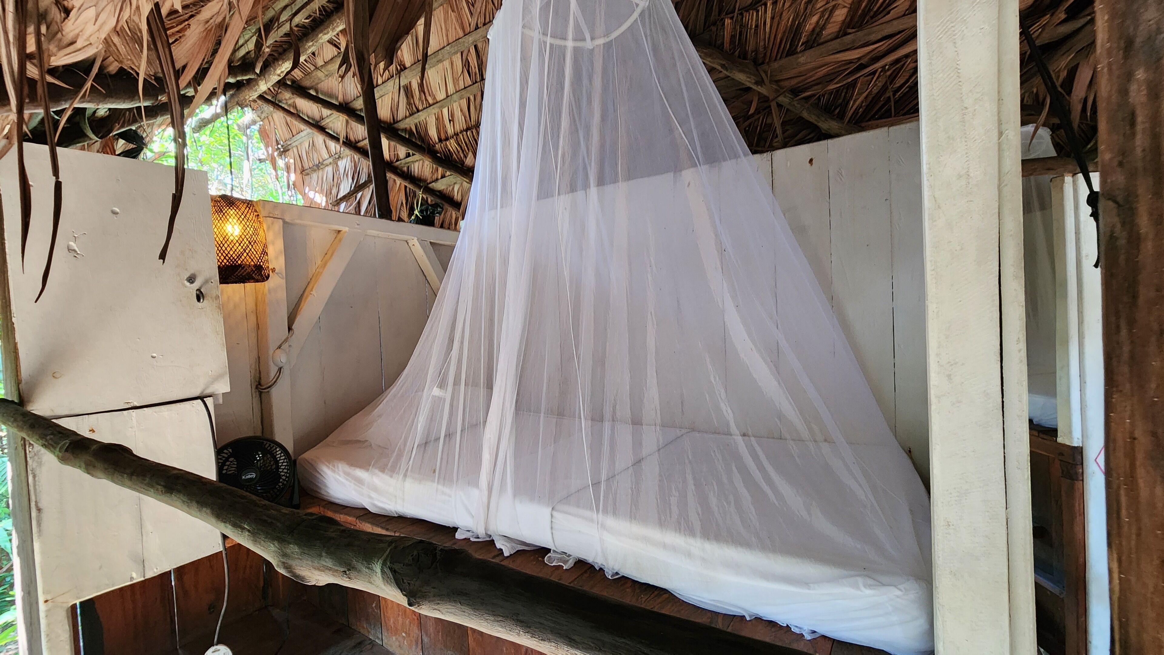 A bed with a mosquito net, a wall-mounted light, and a wooden structure.