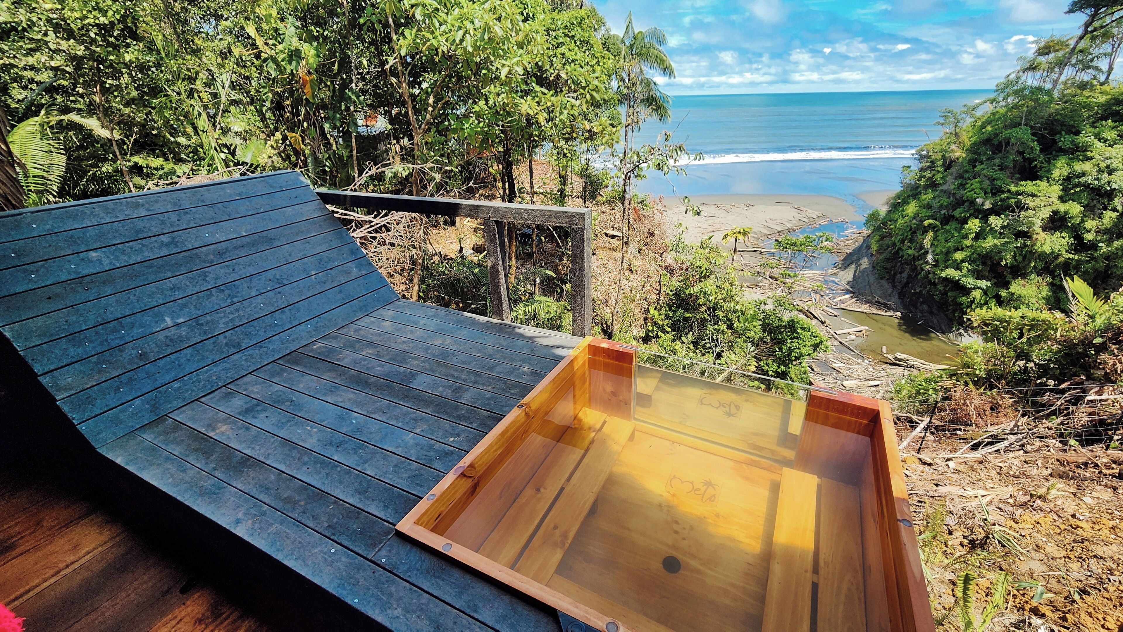 A wooden deck with a glass viewing platform overlooking a beach and ocean.