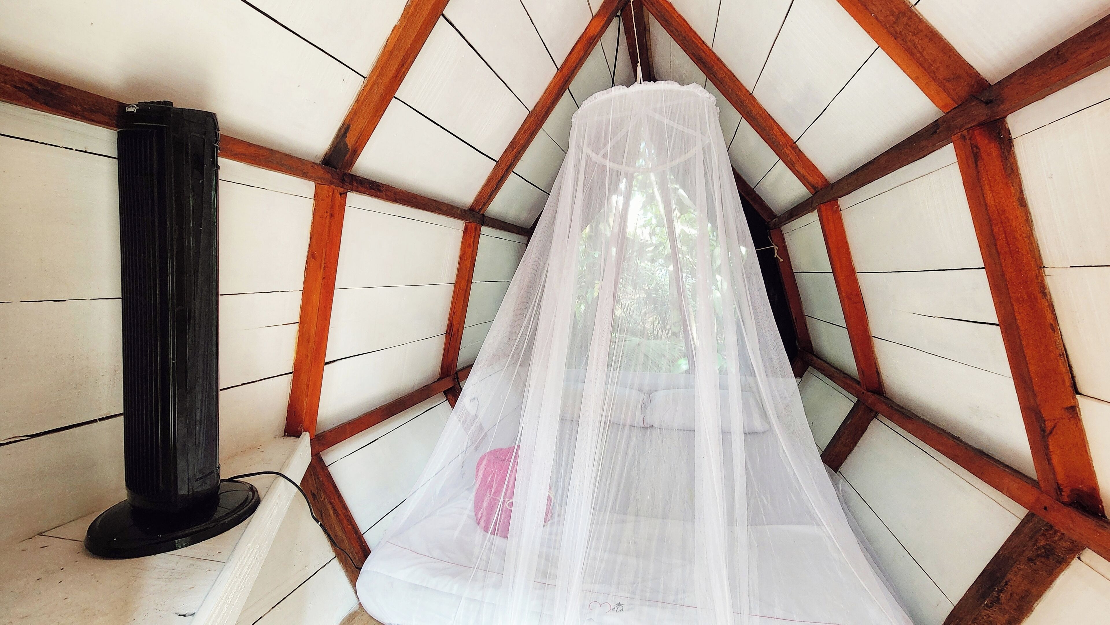 Una habitación con techo inclinado, vigas de madera y un mosquitero.