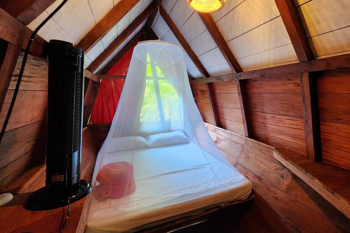 A single bed with a mosquito net in a wooden cabin with a sloped ceiling and a heater.