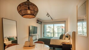A modern hotel room with a large bed, a TV, a dining table, and a view of the city. - Incredible Studio Luxe Tower D902 (Buenos Aires)