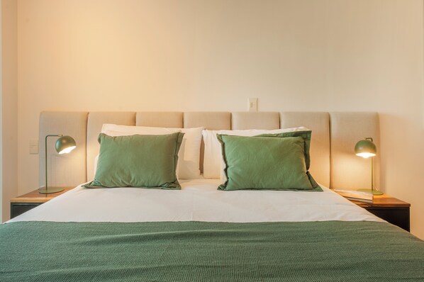 A neatly made bed with green pillows and a green throw blanket, flanked by two bedside lamps on wooden nightstands. - Incredible Studio Luxe Tower D902 (Buenos Aires)
