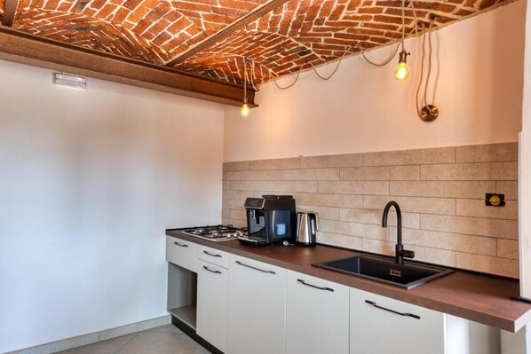 A modern kitchen with a brick ceiling, a gas stove, a coffee maker, and a sink.