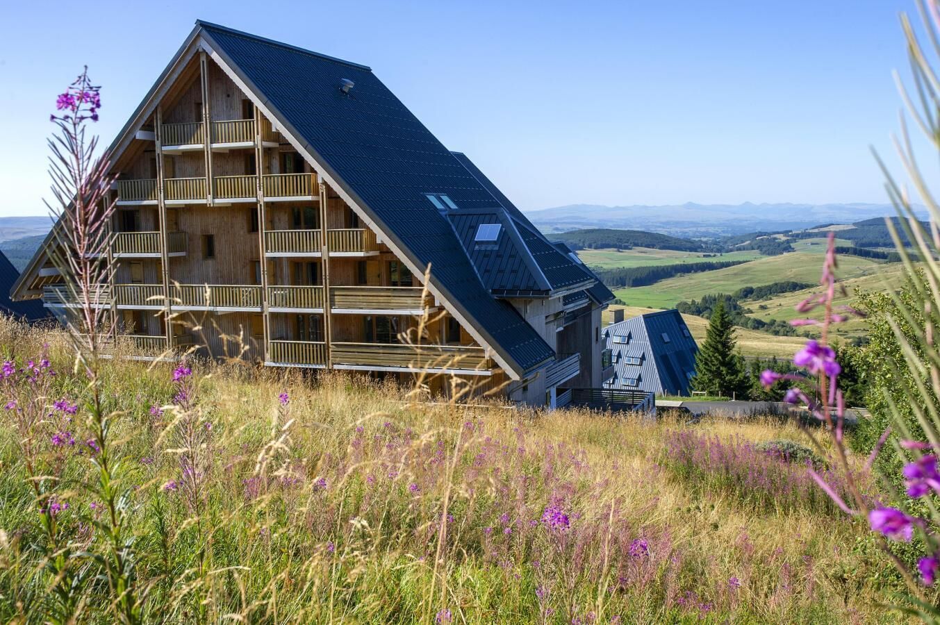 Eine Holzhütte mit geneigtem Dach, mehreren Balkonen und einer schönen Aussicht auf sanfte Hügel.