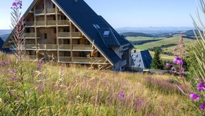 Eine Holzhütte mit geneigtem Dach, mehreren Balkonen und einer schönen Aussicht auf sanfte Hügel.