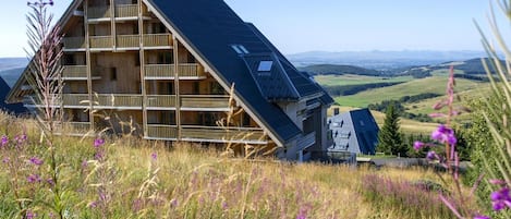 A wooden chalet with a sloped roof, multiple balconies, and a scenic view of rolling hills.