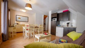 Ein kompakter Wohnbereich mit Essplatz, Küchenzeile und einer Couch mit grünem Kissen.