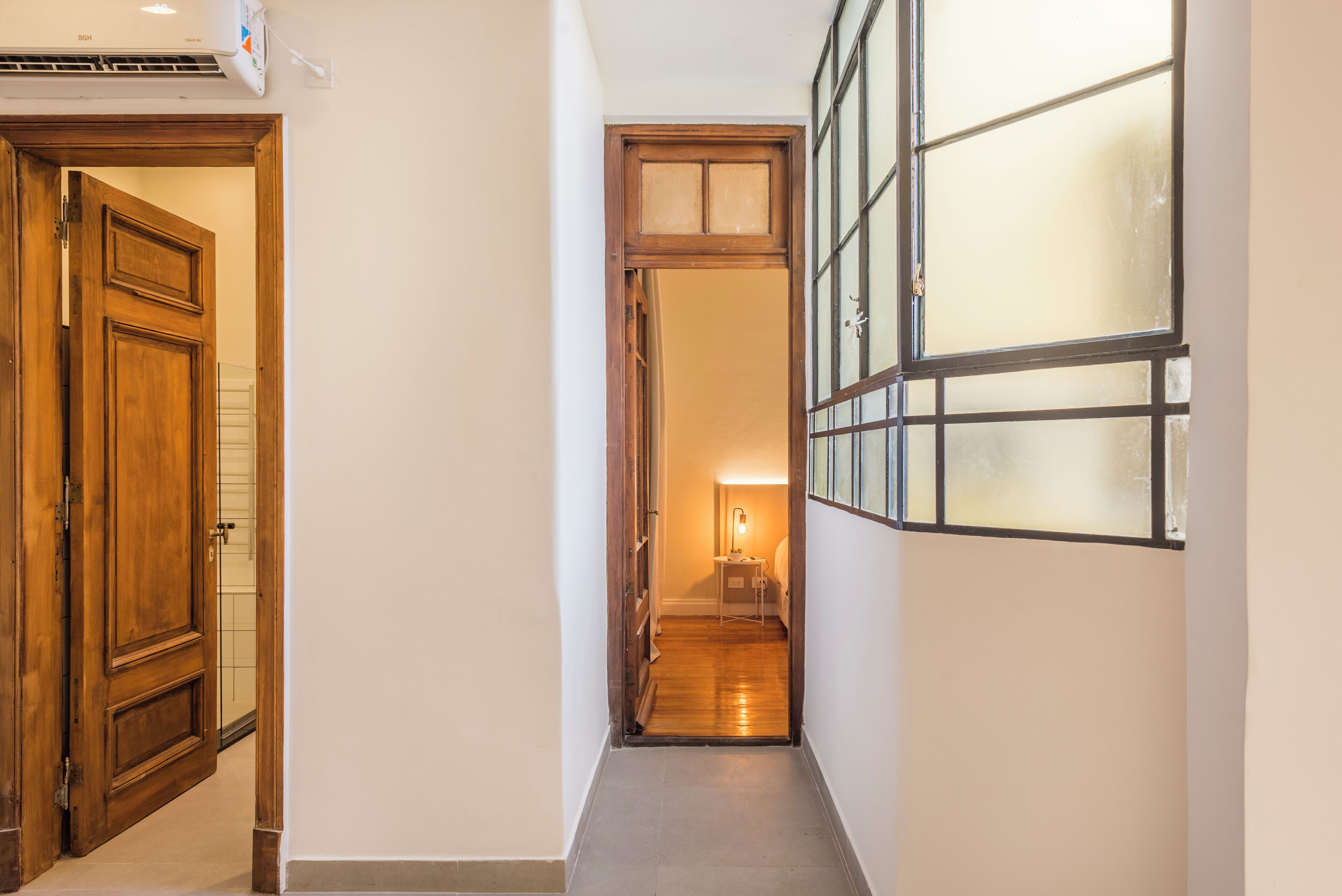 A narrow hallway with a wooden door on the left and a window with frosted glass on the right.