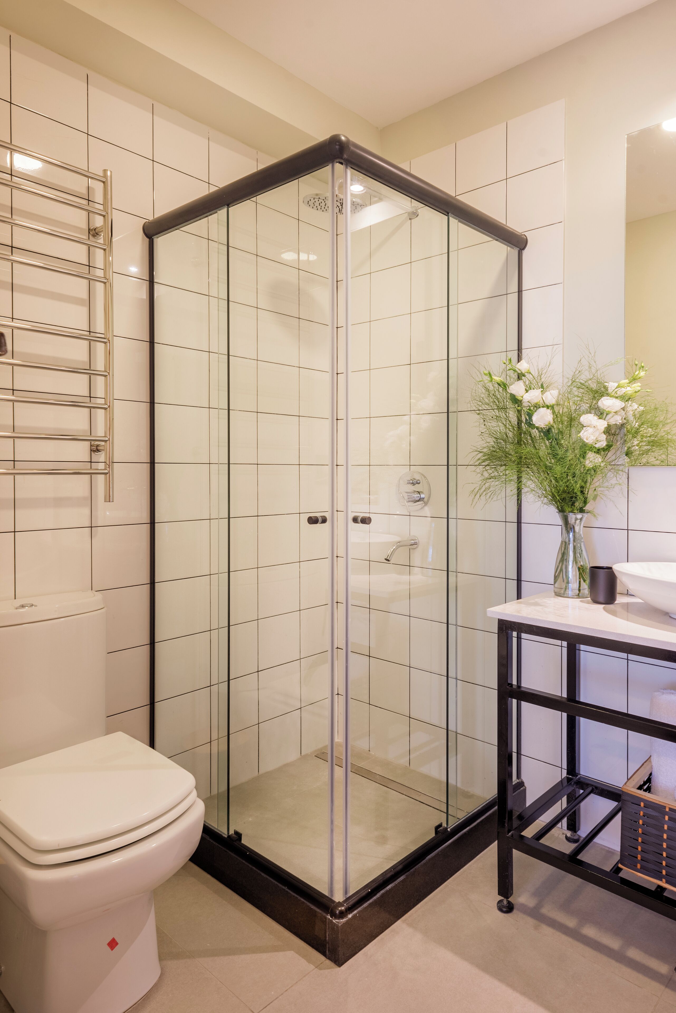 A modern bathroom with a glass-enclosed shower, a white toilet, and a vanity with a vase of flowers.
