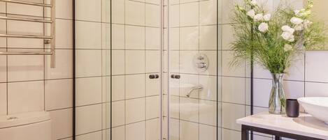 A modern bathroom with a glass-enclosed shower, a white toilet, and a vanity with a vase of flowers.