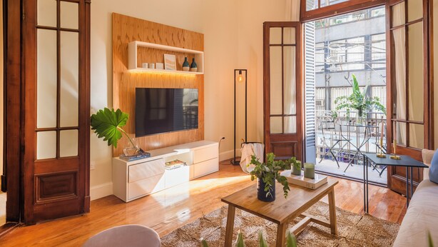 Una sala de estar moderna con un mueble de televisión de madera, un televisor plano grande, un sofá blanco y una mesa de comedor.
