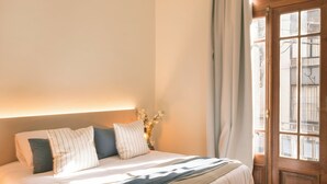 Un dormitorio con cama, piso de madera, una ventana con cortinas y una lámpara colgante.