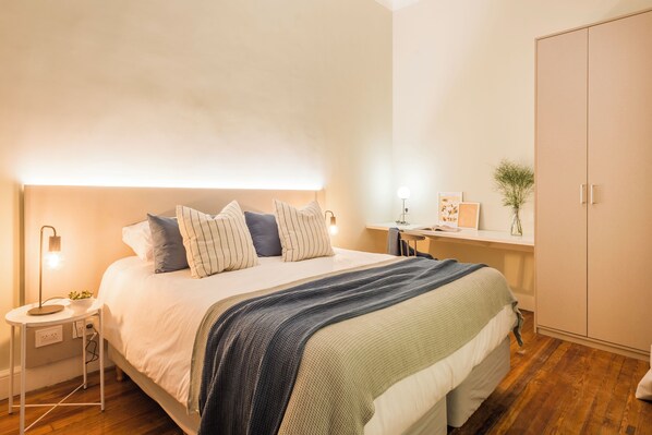 Un dormitorio con una cama grande, mesitas de noche, un escritorio y un armario.