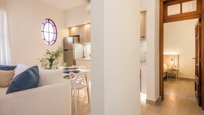Una sala de estar moderna con un sofá, una mesa de comedor y sillas. Hay una zona de cocina con un refrigerador y armarios.