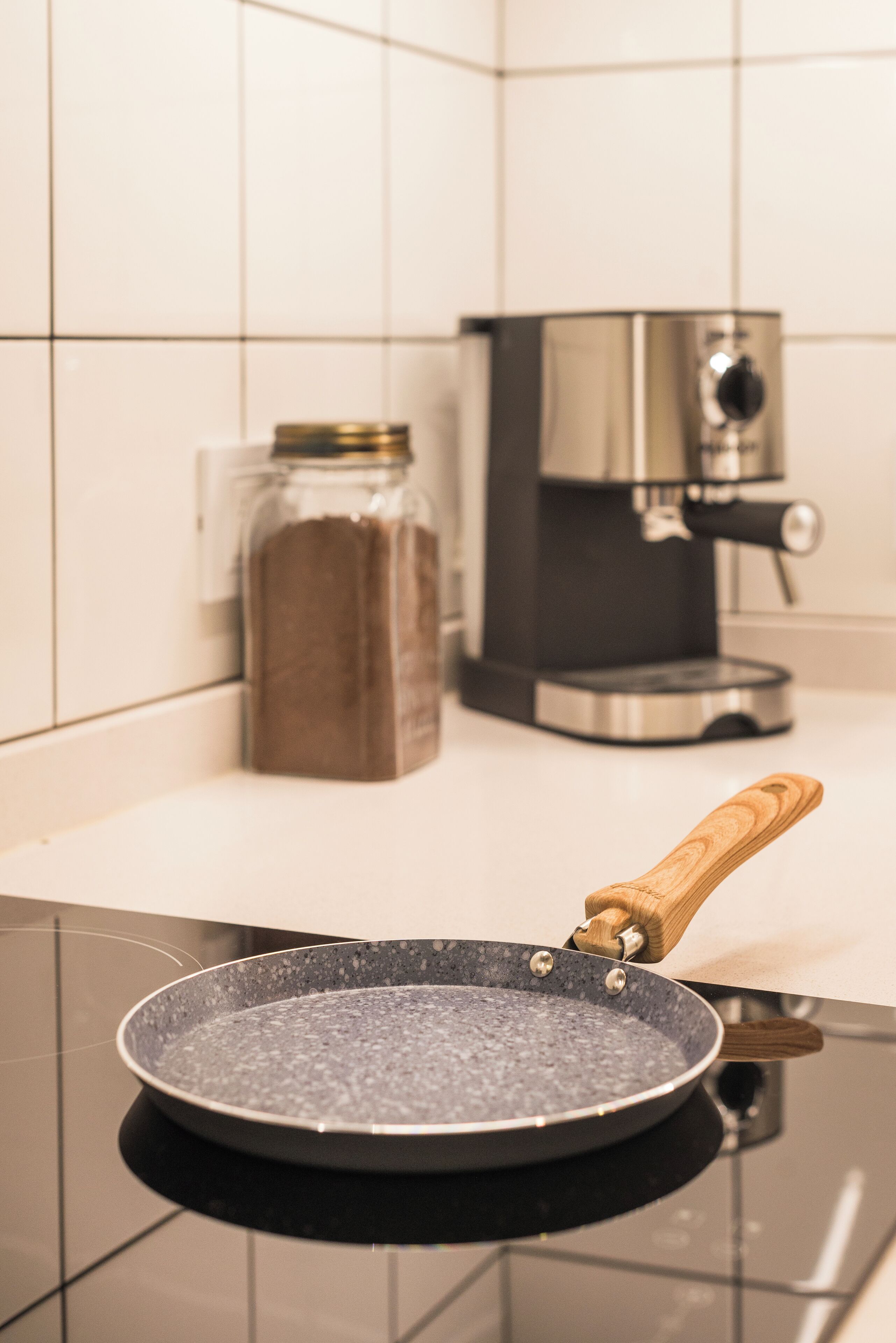 Una cocina con una cafetera, un tarro de especias y una sartén sobre la hornilla.