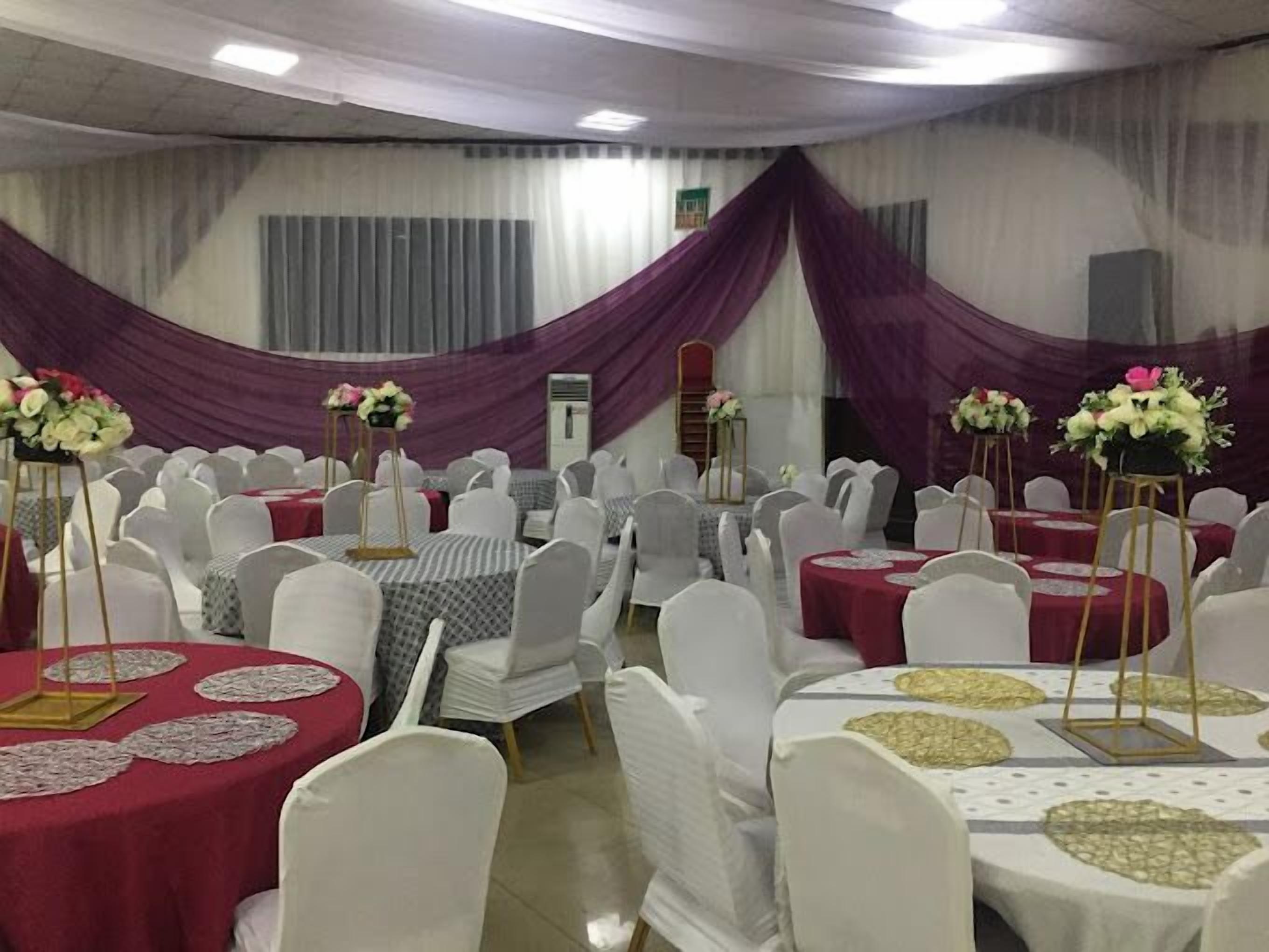 Un salón de banquetes con mesas redondas cubiertas con manteles blancos y rojos, sillas blancas y centros de mesa con flores.