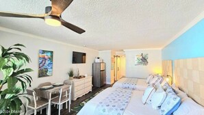 Een slaapkamer met een bed, een bureau, een stoel, een plafondventilator en een plant.