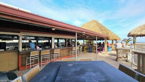 Een openluchtrestaurant met een overdekt zitgedeelte, rieten parasols en uitzicht op het strand.