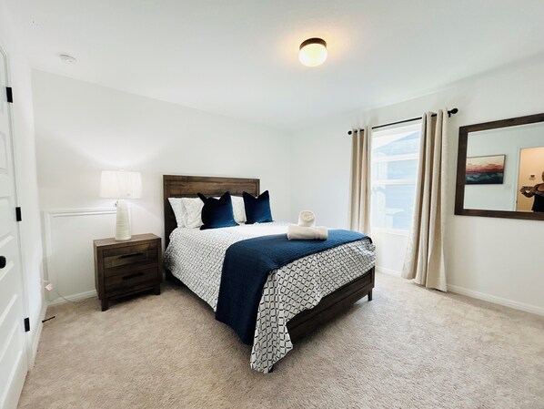 Une chambre à coucher comprenant un lit, une table de chevet, une lampe, une fenêtre avec des rideaux et un miroir fixé au mur.