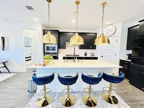 Une cuisine moderne dotée d’un îlot central, de tabourets de bar et de luminaires suspendus.