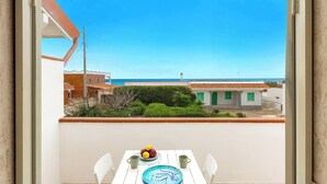 Ein Balkon mit Tisch für zwei Personen, Blick auf das Meer und ein Gebäude mit einer grünen Tür im Hintergrund.