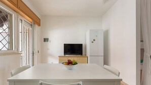Eine kleine Küche mit einem weißen Kühlschrank, einem Fernseher auf einer Holzkassette und einem Esstisch mit Stühlen.