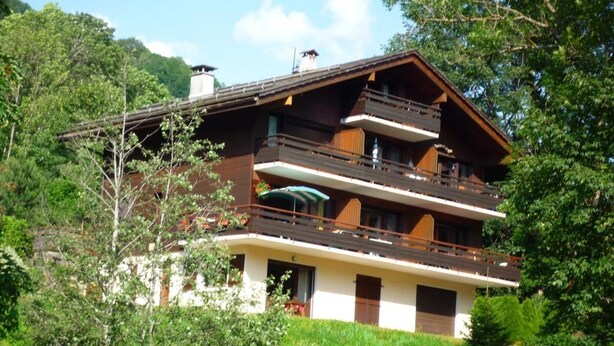Um chalé de vários andares com varandas, rodeado por vegetação exuberante.