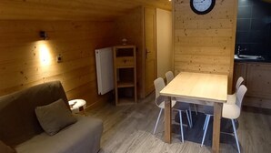 Interior acolhedor de uma cabana de madeira, com uma mesa de jantar, cadeiras, um sofá e um relógio na parede.