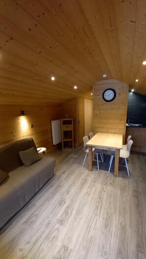 Ein gemütliches Holzblockhaus-Interieur mit einem Esstisch und Stühlen, einer Couch und einer Uhr an der Wand.